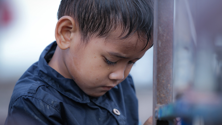 A young boy in Cambodia lowers his head sadly