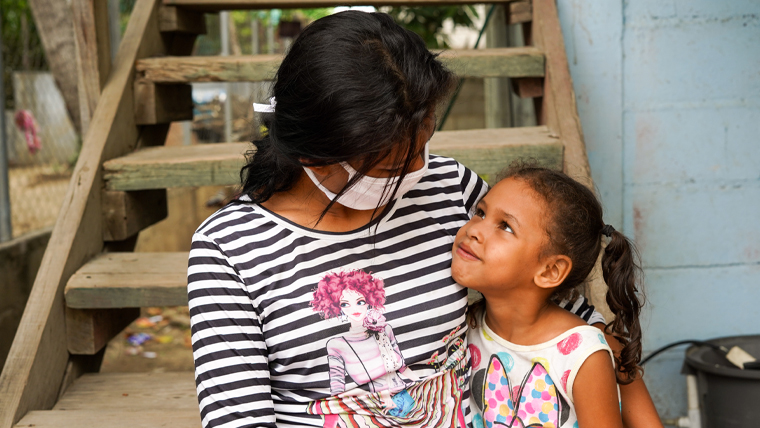 Ana (wearing a face mask), hugs her 5-year-old daughter, Briana, on the steps outside the home in Honduras