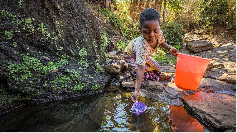 Ireen at the water hole, scooping water into her bucket