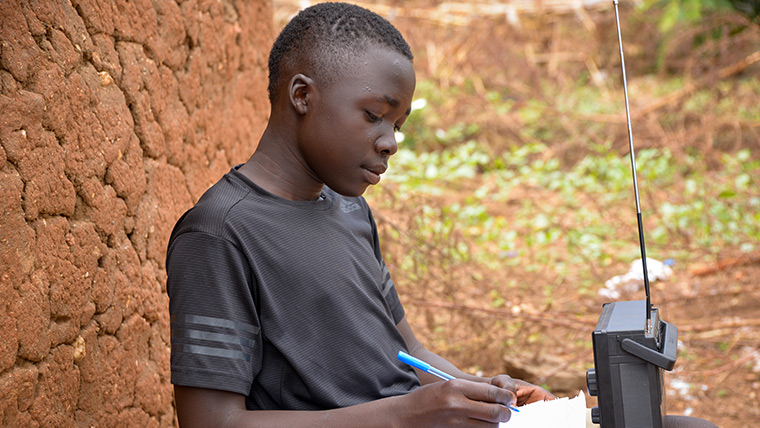 15-year-old Simon uses a radio to keep studying in Bidibidi refugee settlement in Uganda during coronavirus.